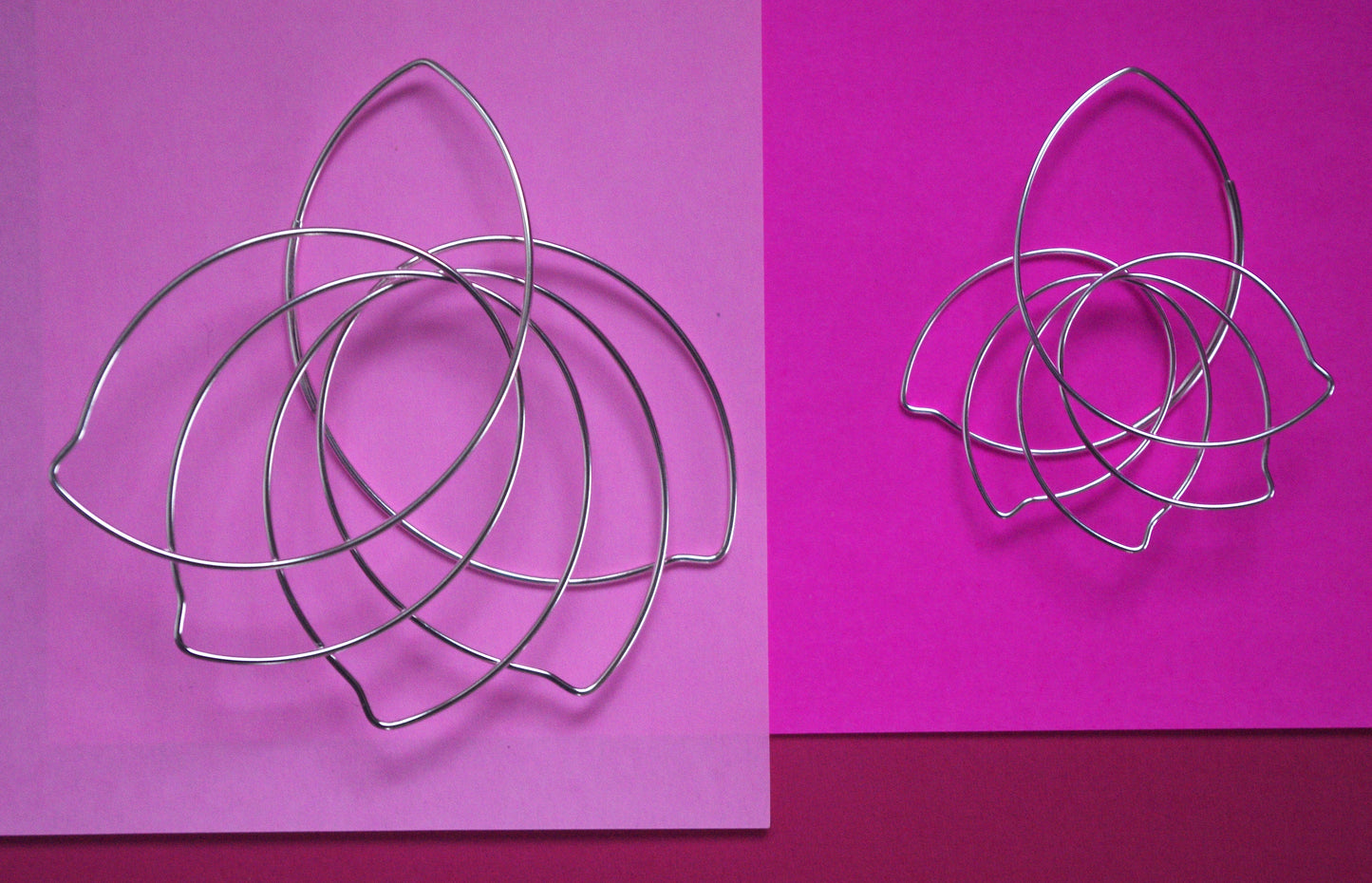 Two models of statement earrings by Belgian-American jewelry designer Hannah Tomoko. Both designs are large but light and they close in a nearly invisible tubing to enhance the continuity of the design. Both earrings are made of one continuous sterling silver wire that is meticulously curved and bent. This particular model is like a a wave of curved flower petals or fanning bird feathers. The first earring is a true statement earring, while the second is a scaled down version of the first.